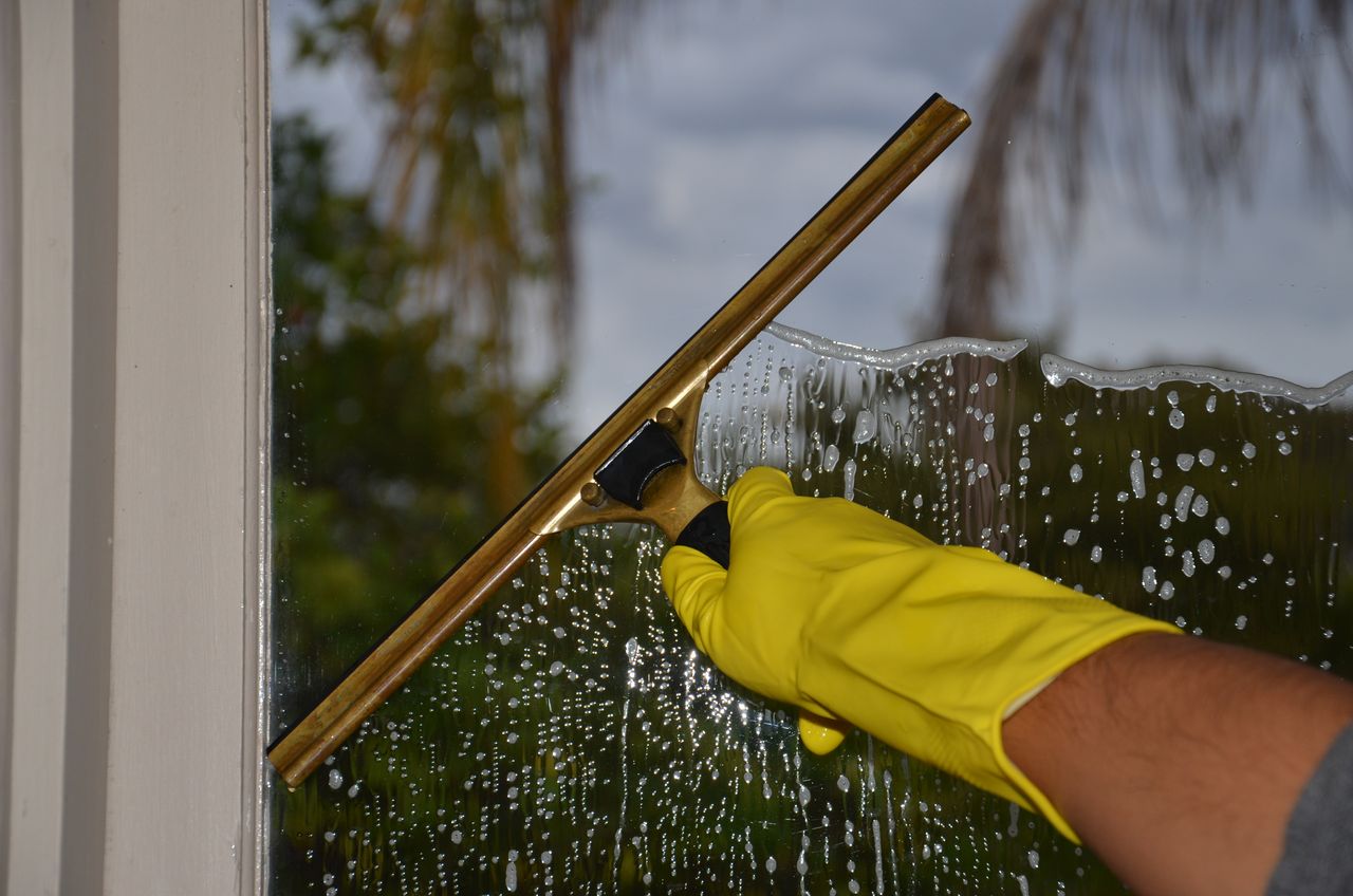 services-02 Close-up of hand cleaning window with squeegee outdoors using yellow gloves.